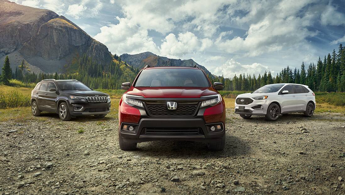 Front view of 2019 Honda Passport in Deep Scarlet Pearl parked on dirt turnout with competitor SUVs and mountains in background