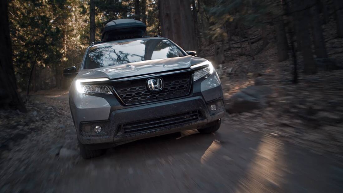 Front view of the 2019 Honda Passport Elite in Lunar Silver Metallic, with accessory roof box, driving on dirt road in forest.