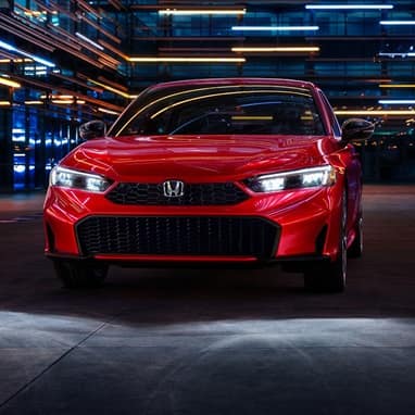 2027 Honda Civic Sedan Sport Touring Hybrid in Rallye Red front view with headlights on (Compact Sedan)